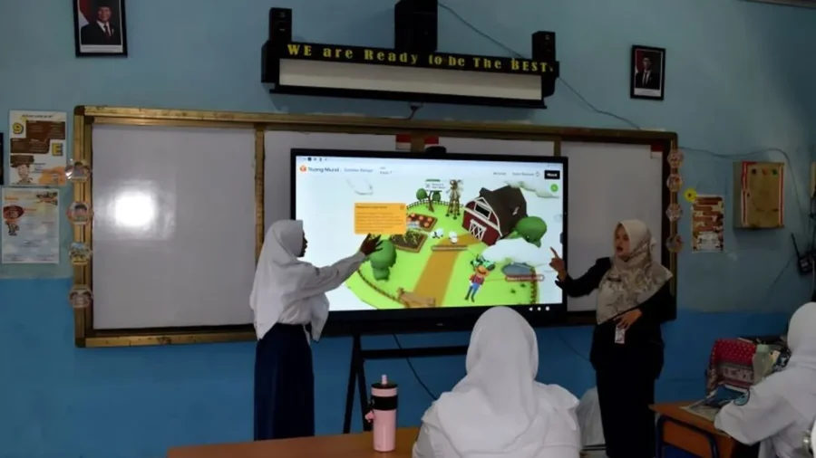 Seorang guru dan siswi menunjuk layar interaktif di kelas saat pembelajaran digital berlangsung.