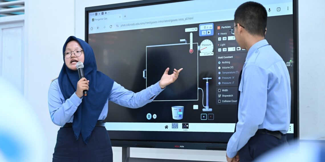 Guru menjelaskan teori kinetik gas kepada siswa menggunakan papan interaktif digital di ruang kelas sekolah menengah.